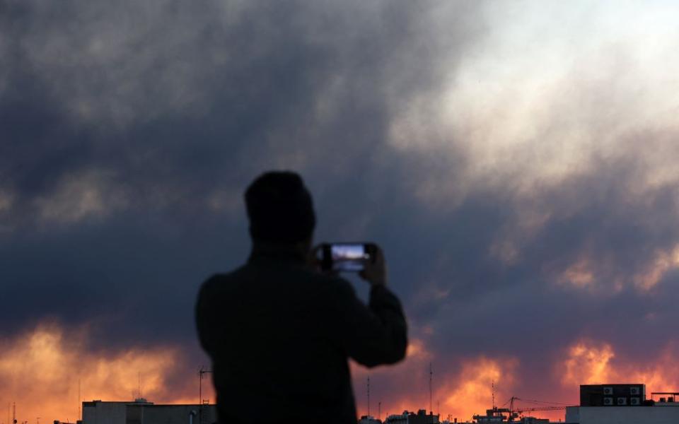 A person uses a phone as smoke rises following an explosion in Tehran, Iran, March 3. Israel and the U.S. launched strikes on Iran Feb. 28. (OSV News/West Asia News Agency via Reuters/Majid Asgaripour)