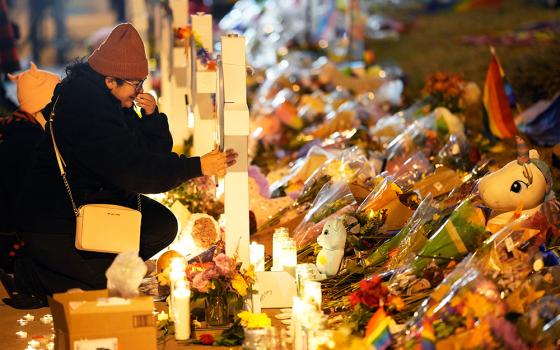 A woman in a black coat and knit hat cries as she knees next to a makeshift memorial during a candlelight vigil