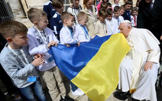 Pope Francis kisses a Ukrainian flag carried by a group of Ukrainian children attending his weekly general audience in St. Peter's Square at the Vatican April 10, 2024. The pope prayed during the audience for peace in Ukraine, in the Holy Land and in Myanmar. (CNS/Vatican Media)
