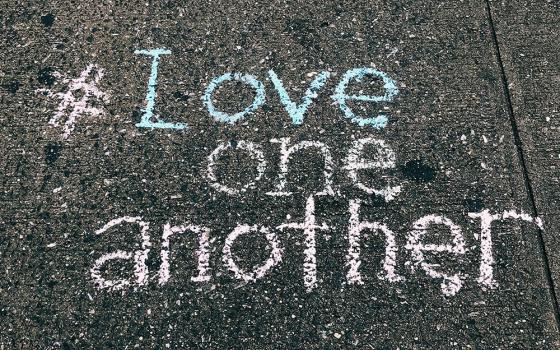 A concrete floor displays the words "#Love one another" written in chalk (Unsplash/Jon Tyson)