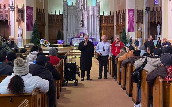 Cardinal Blase Cupich of Chicago addresses migrants at the Migrant Ministry's first location at St. Catherine of Siena-St. Lucy Church in Oak Park, Illinois, in a December 2023 photo. Program organizer Celine Woznica is pictured at the right. (Courtesy of Migrant Ministry)
