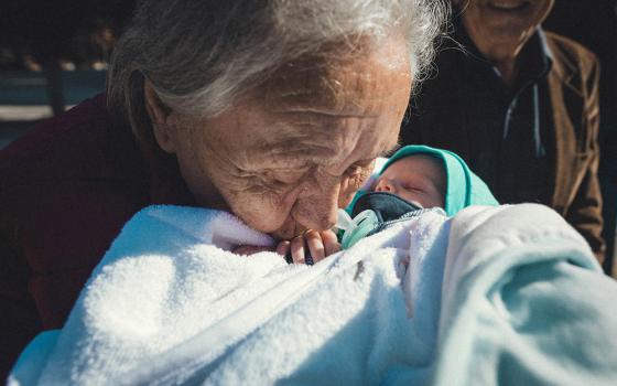 Grandmother kisses a baby on the hand (Unsplash/Tamara Govedarovic)