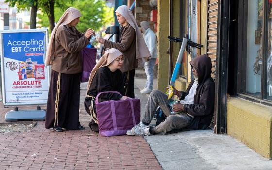 Sister Giovana of the Most Holy Name of Jesus (squatting) joins Sister Samaritan of Scourged Love (left) and Sister Maria Clara of the Crucified in giving food to a man near Lexington Market in Baltimore May 3, 2023. (OSV News/Catholic Review/Kevin J. Parks)
